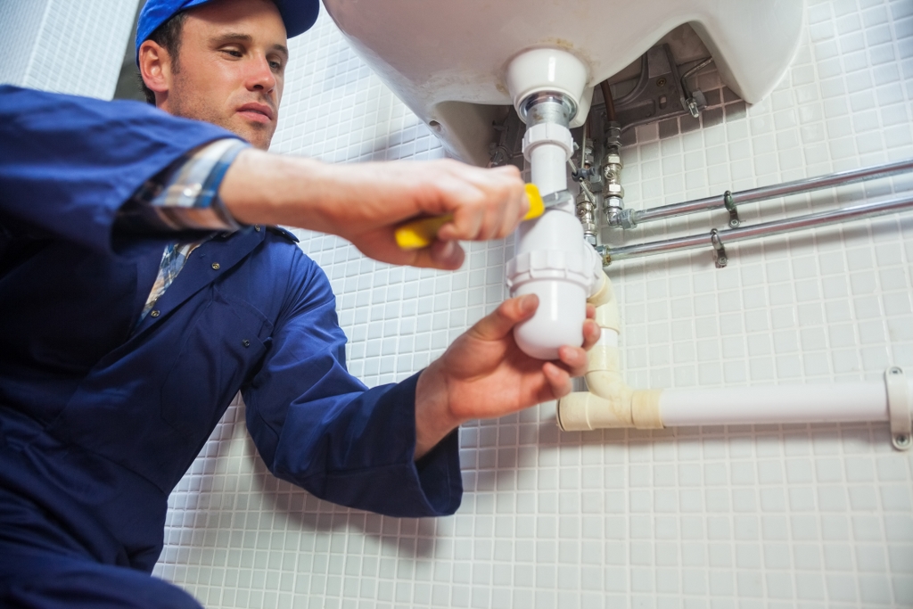 Frowning plumber repairing sink in public bathroom Frowning plumber repairing sink in public bathroom